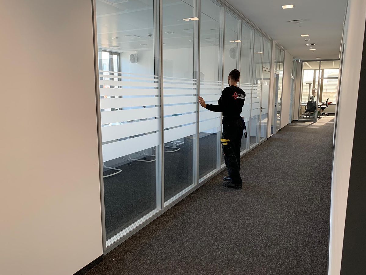 Monteur bringt Sichtschutzstreifen aus Milchglasfolie an gläsernen Bürotrennwänden an