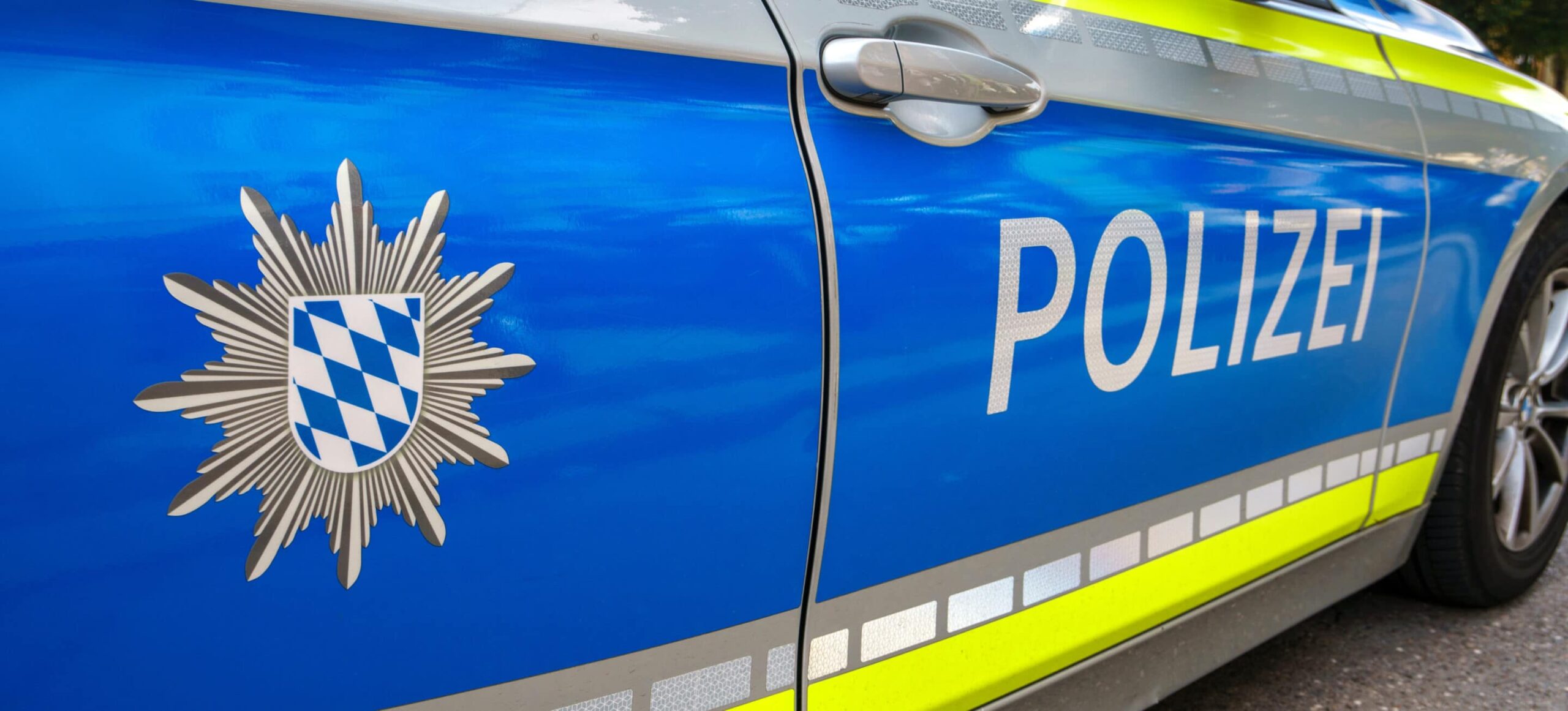 Polizeifahrzeug mit blau-gelber Folierung, reflektierenden Streifen und Polizei-Schriftzug an der Fahrzeugseite